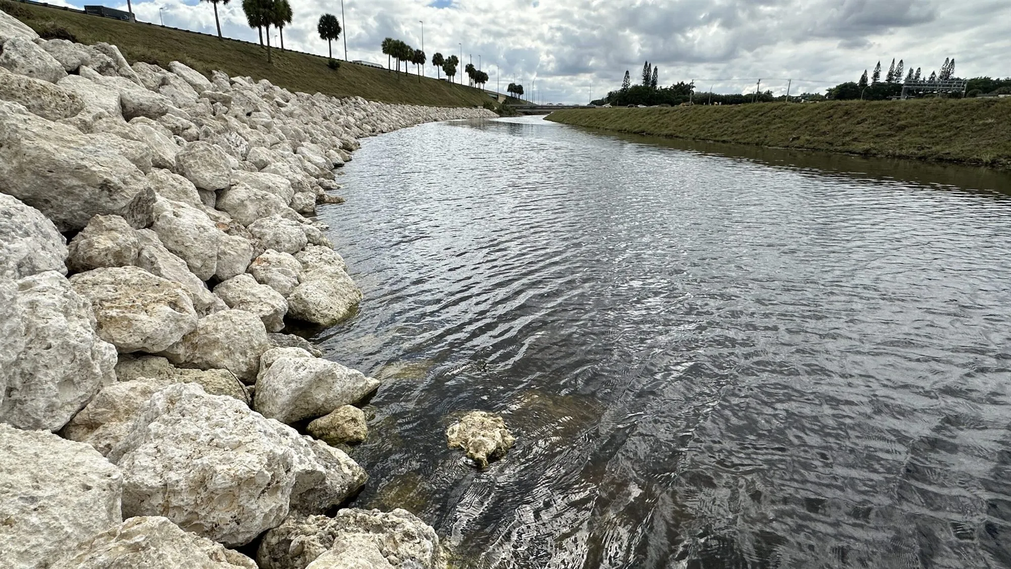 Pale boulders piled along the bank of a canal, from the top of the slope down into the water.